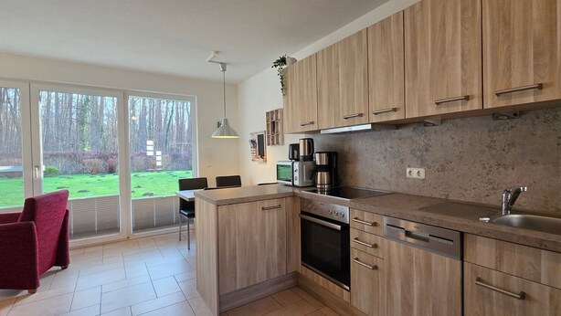 A modern kitchen with wooden cabinets, a built-in oven, and a large window overlooking a grassy area. - Apartment KWi 46 ground floor - 2-room apartment for 4 pers. on the ground floor, incl. 4 bicycles (Gelbensande)