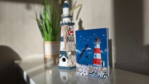 A table with a decorative lighthouse model, a framed picture of a lighthouse, and a potted plant. - Apartment KWi 46 ground floor - 2-room apartment for 4 pers. on the ground floor, incl. 4 bicycles (Gelbensande)