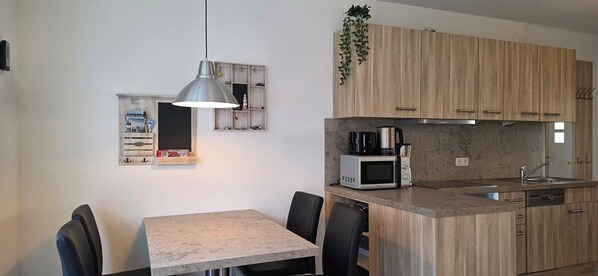 A compact kitchen with a dining area, featuring a microwave, coffee maker, and wooden cabinets.