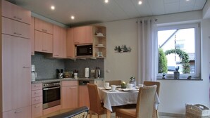Une cuisine avec des meubles de rangement roses, un four à micro-ondes et un coin repas avec une table dressée pour quatre personnes.