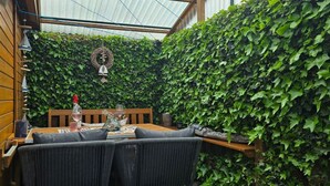 Un coin accueillant avec un banc et une table en bois, entouré de murs couverts d’une luxuriante végétation de lierre.