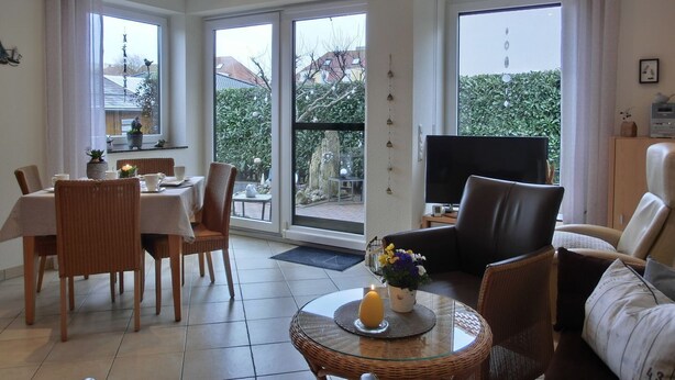 Un salon moderne avec une table à manger en verre, des chaises en osier, un canapé et un téléviseur.