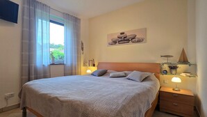 Une chambre à coucher bien rangée, avec un lit, des lampes de chevet, un téléviseur fixé au mur et une fenêtre avec des rideaux.