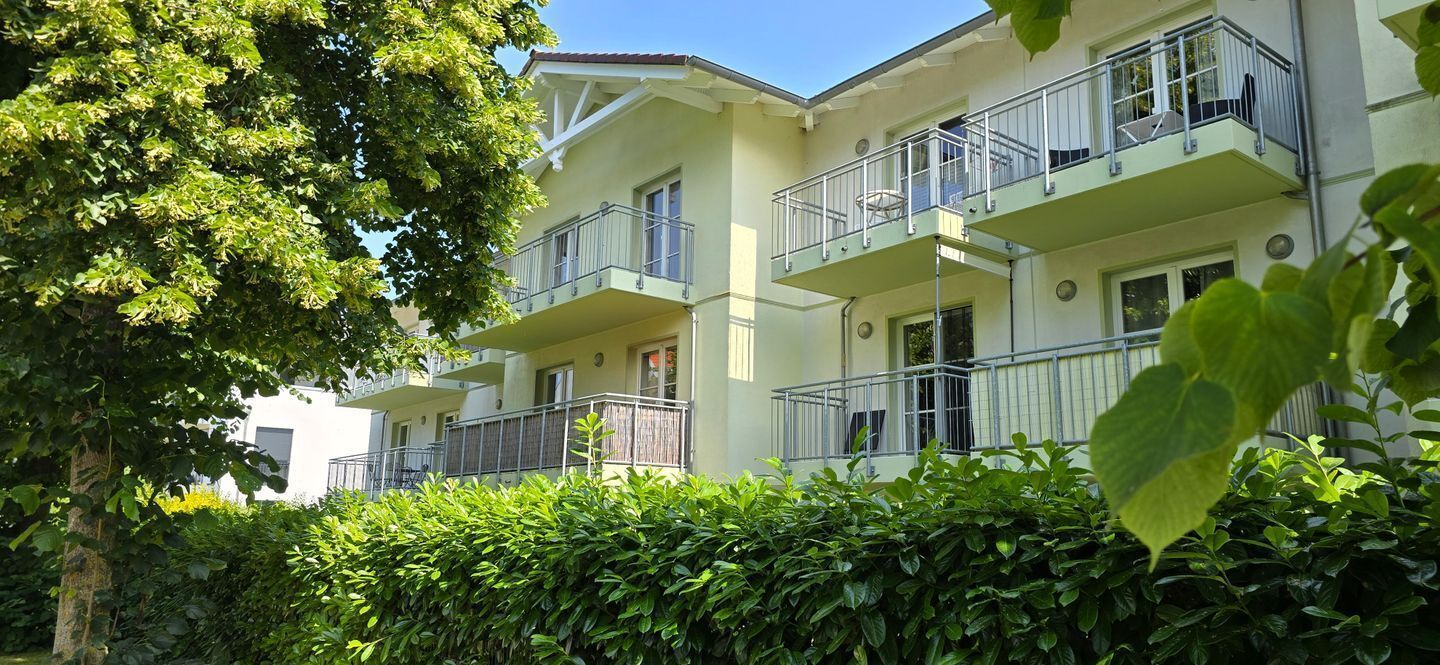 Un edificio residencial de varios pisos con balcones, rodeado de abundante vegetación.