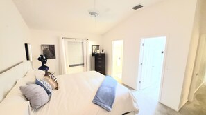 Une chambre à coucher avec un lit, une commode, une porte et une fenêtre avec des stores.
