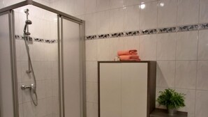 Un baño con cabina de ducha de vidrio, un mueble blanco con cajones y un pequeño estante con una planta.