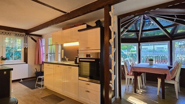 Une cuisine équipée d’appareils électroménagers modernes, un coin repas avec une table et des chaises, et une vue sur l’extérieur grâce à de grandes fenêtres.