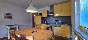 A compact kitchen with yellow cabinets, a wooden dining table, and a pendant light.