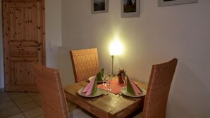 Zona pranzo con tavolo in legno apparecchiata per due persone, sedie in vimini e lampada da tavolo.