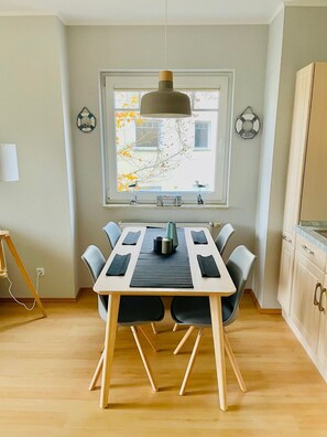 Un coin repas avec une table dressée pour quatre personnes, un luminaire suspendu et une vue sur un arbre à travers la fenêtre.