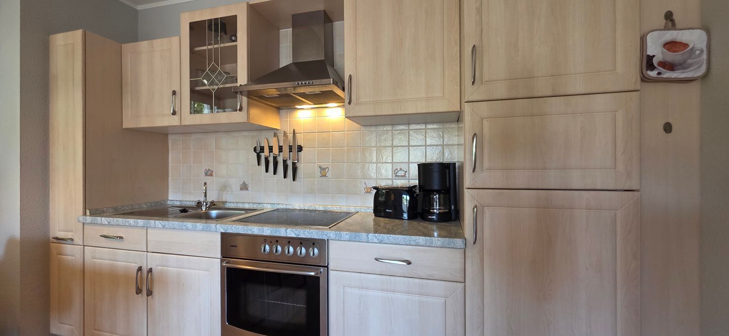 A kitchen with light wood cabinets, a stainless steel range hood, a coffee maker, and a knife block.
