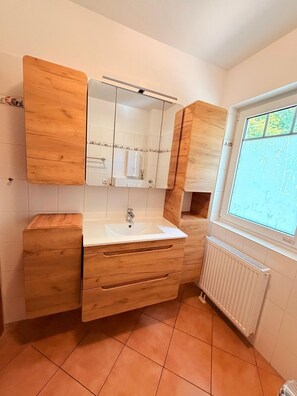 Une salle de bain avec un meuble-lavabo en bois, un lavabo blanc et une fenêtre donnant sur un paysage verdoyant.