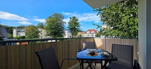 Ein Balkon mit Tisch und Stühlen, ein Holzzaun und Gebäude im Hintergrund.