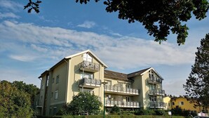 A multi-story residential building with balconies, a paved driveway, and parked cars.