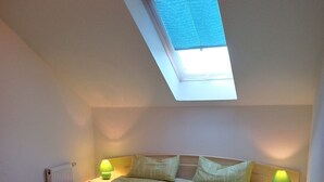 A bedroom with a skylight, a large bed, two bedside tables with lamps, and a radiator.