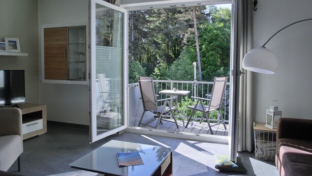 Een moderne woonkamer met een glazen deur die leidt naar een balkon, een flatscreen televisie, een bank, een salontafel en een lamp.