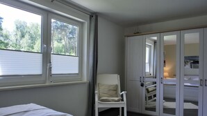 Een slaapkamer met twee bedden, een stoel, een kledingkast en een raam met zonwering.