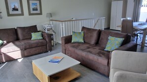 Een moderne woonkamer met twee bruine banken, een witte salontafel en een eethoek met een tafel en stoelen.
