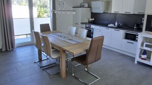 Een moderne keuken met witte kasten, een eettafel met stoelen en een groot raam met gordijnen.