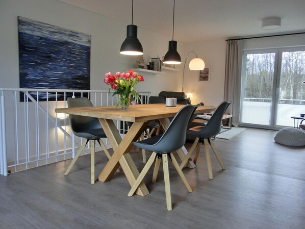 A dining area with a wooden table and black chairs, a vase of flowers, and pendant lights.
