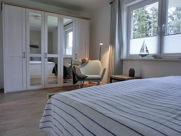 A bedroom with a bed, a chair, a wardrobe, and a window with a sailboat decoration.