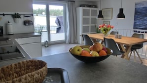 Una cocina moderna con comedor, un ventanal grande y un cuenco de fruta sobre la mesa.