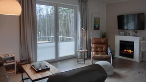 Una sala moderna con chimenea, un sillón de cuero, un televisor de pantalla plana y un amplio ventanal corredero que da a un balcón.
