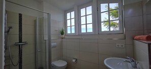 A bathroom with a glass-enclosed shower, a toilet, a sink, and a window with a view. - FH T 1c Vacation Home - a townhouse with approximately 95 m² of living space, sleeping 6 people (Graal-Müritz)