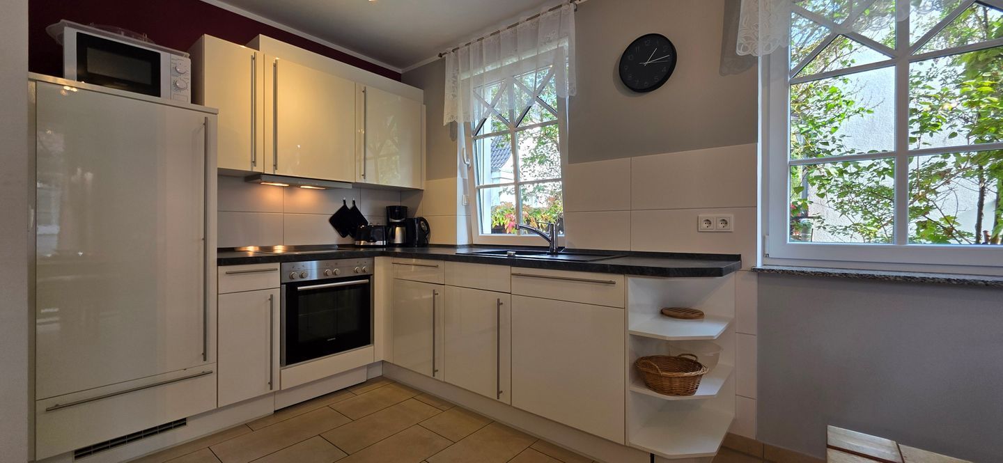 A kitchen with white cabinets, a microwave, a stove, and a window with a view of greenery.