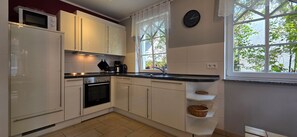 A kitchen with white cabinets, a microwave, a stove, and a window with a view of greenery. - FH T 1c Vacation Home - a townhouse with approximately 95 m² of living space, sleeping 6 people (Graal-Müritz)