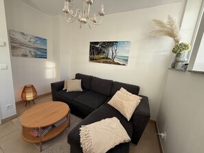 Un salon moderne avec un canapé d’angle gris foncé, une table basse ronde en bois et deux tableaux accrochés au mur représentant des paysages naturels.
