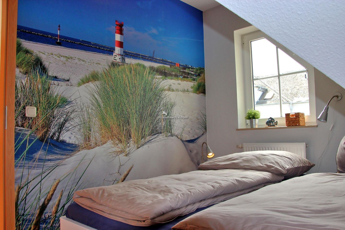 Une chambre avec un grand décor mural représentant une plage, une fenêtre donnant sur la mer et une lampe de chevet.
