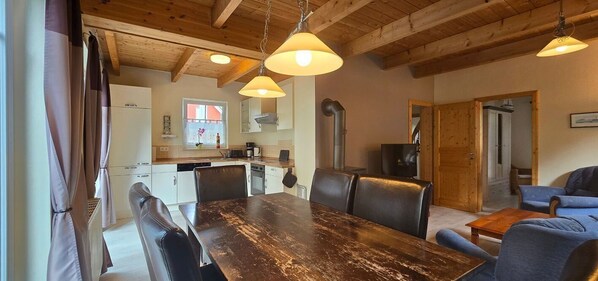 Un coin repas avec une table et des chaises en bois, une cuisine à l’arrière-plan et un plafond en bois.