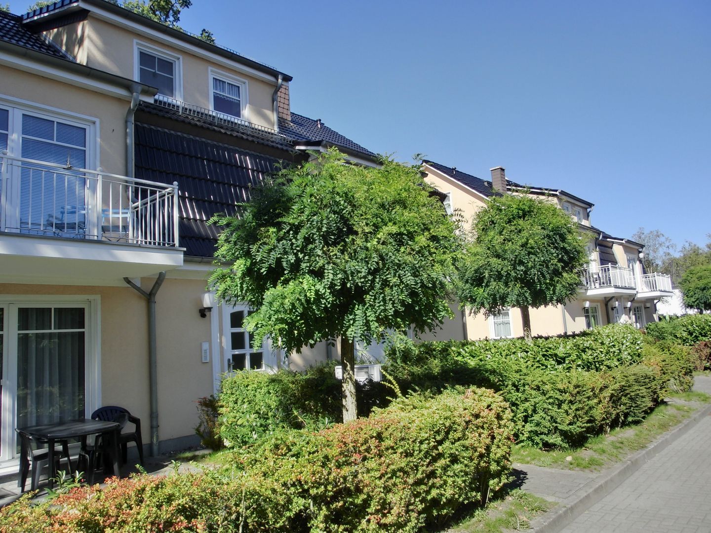 A row of two-story houses with balconies, a paved pathway, and well-maintained greenery.