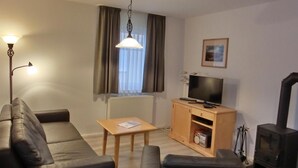 Una sala de estar con sofá, una mesa de centro, un televisor sobre un mueble de madera, chimenea y ventana con cortinas.