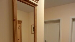 Un pasillo con un espejo de marco de madera, una puerta blanca y un suelo de baldosas.