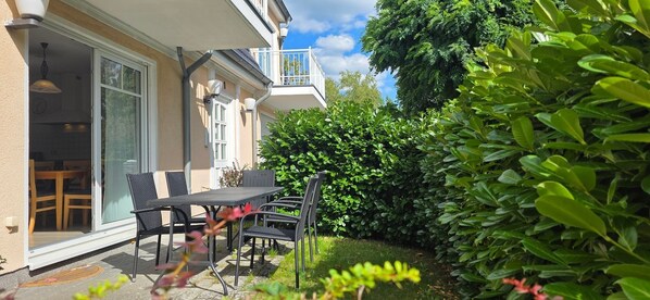 Une terrasse avec une table et des chaises, une porte-fenêtre coulissante et un balcon doté d’une balustrade.