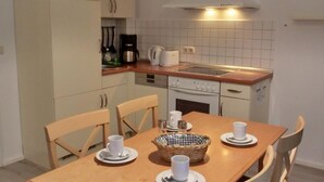 Cocina compacta con una mesa de comedor para cuatro, equipada con electrodomésticos básicos y una lámpara colgante.