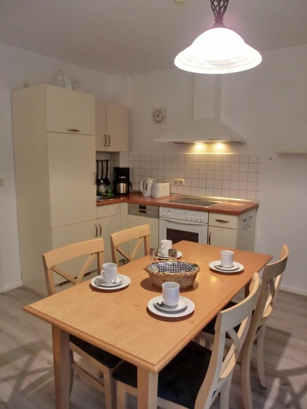 Une cuisine compacte avec une table à manger pour quatre personnes, équipée d’appareils électroménagers de base et d’un luminaire suspendu.