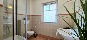 Une salle de bain avec une douche à parois de verre, des toilettes, une fenêtre et un lavabo agrémenté d’une plante.