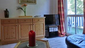 A living room with a TV, wooden cabinets, a red candle, and a window with a view of trees.