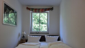 A bedroom with a bed, a window with a view of trees, a lamp, and a painting on the wall.
