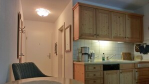 A compact kitchen with wooden cabinets, a coffee maker, and a dining table with a placemat.