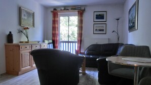 A living room with a black sofa, a dining table with chairs, a wooden cabinet, and a window with curtains.