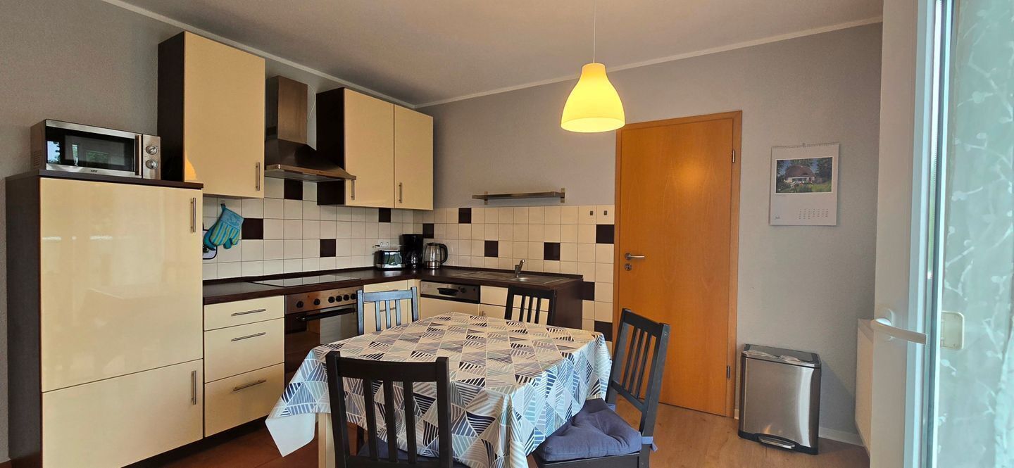 A compact kitchen with a microwave, stove, and sink. There is a dining table with chairs and a hanging light fixture.