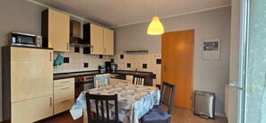A compact kitchen with a microwave, stove, and sink. There is a dining table with chairs and a hanging light fixture.