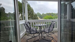 Un espace extérieur abrité, doté d’une table et de chaises, d’une rambarde blanche et offrant une vue sur les arbres et les bâtiments.
