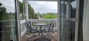 A covered outdoor area with a table and chairs, a white railing, and a view of trees and buildings.