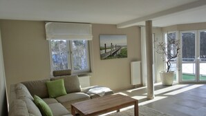 Un salon moderne avec un canapé, une table basse et une grande fenêtre donnant sur une plage et une jetée en bois.