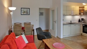 A compact living space with a kitchenette, a dining area with a table and chairs, and a sofa with cushions. - Vacation apartment LVC4 - 2-room apartment for 4 pers. with WLAN (Graal-Müritz)